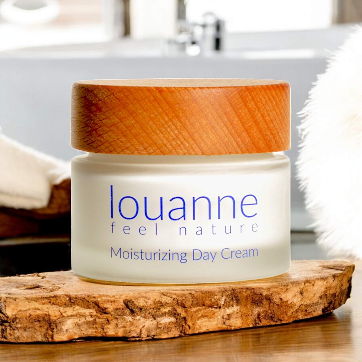 Louanne feel nature – palmölfreie Moisturizing Day Cream in einem edlen Glastiegel mit Holzdeckel, präsentiert auf einer Holzscheibe vor natürlichem Badezimmer-Hintergrund